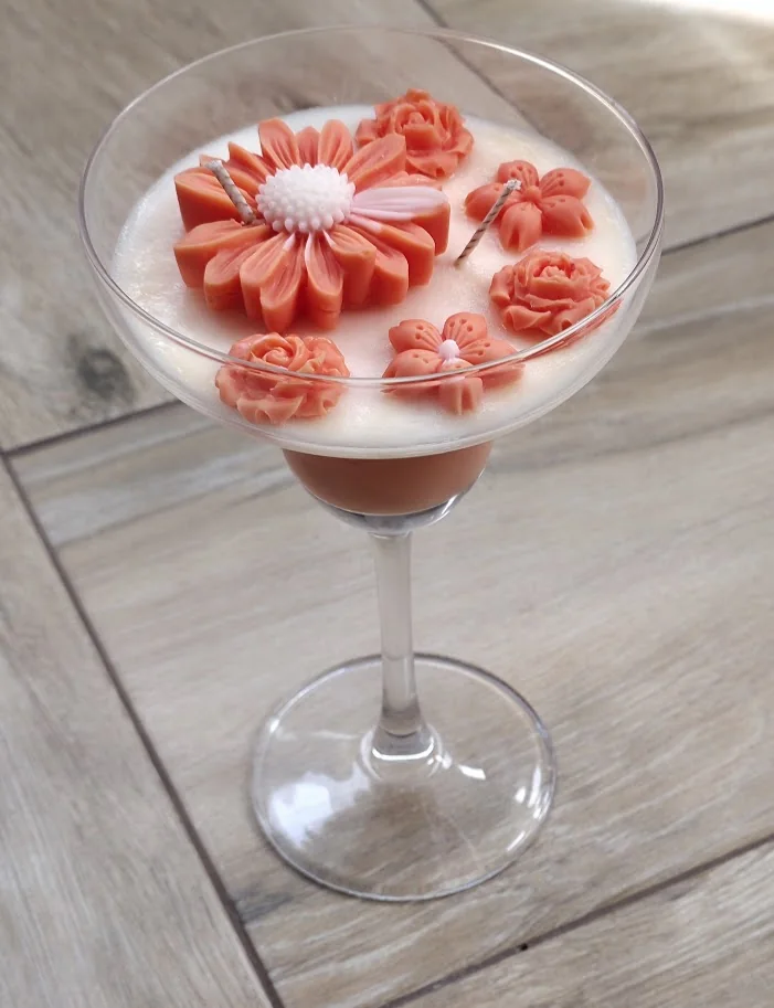 Copa de cóctel de cristal con vela blanca y flores naranjas de cera